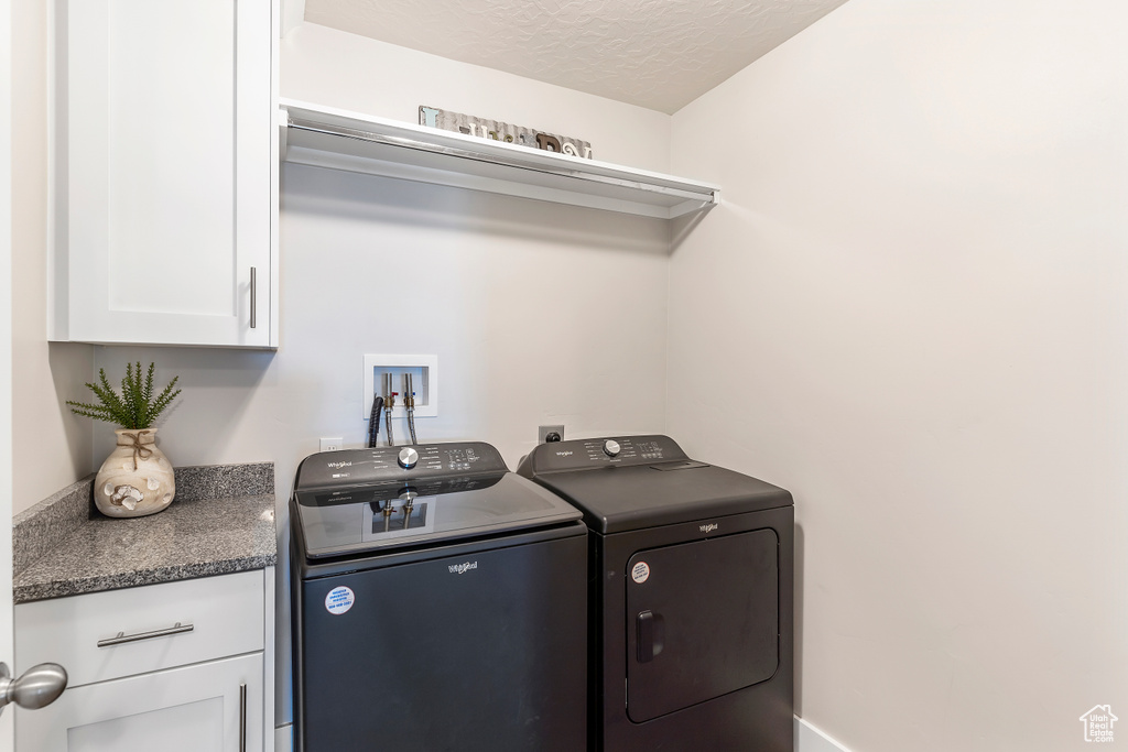 Laundry room featuring washer and clothes dryer, cabinet space, and a textured ceiling