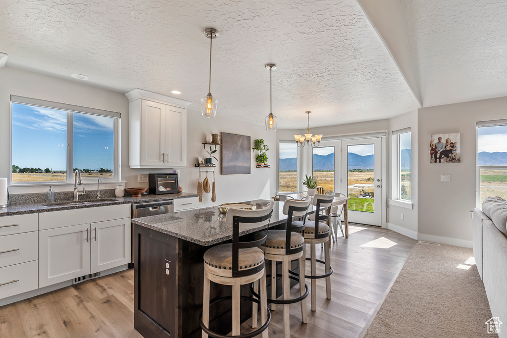 Kitchen featuring a textured ceiling, a kitchen breakfast bar, dark stone countertops, a chandelier, and white cabinetry
