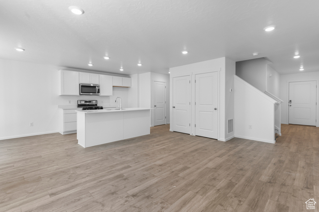 Kitchen featuring stainless steel appliances, open floor plan, recessed lighting, white cabinetry, and a kitchen island with sink