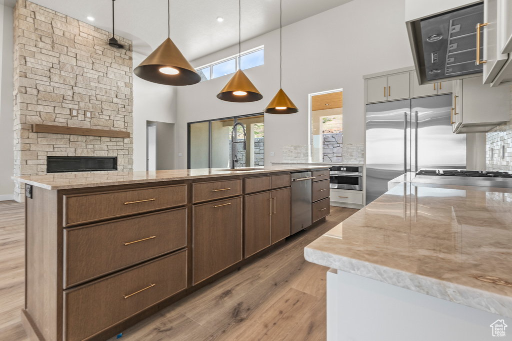 Kitchen featuring appliances with stainless steel finishes, a towering ceiling, light wood-style flooring, light stone countertops, and a fireplace