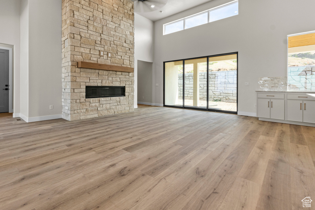 Unfurnished living room featuring a high ceiling, healthy amount of natural light, light wood finished floors, and a stone fireplace