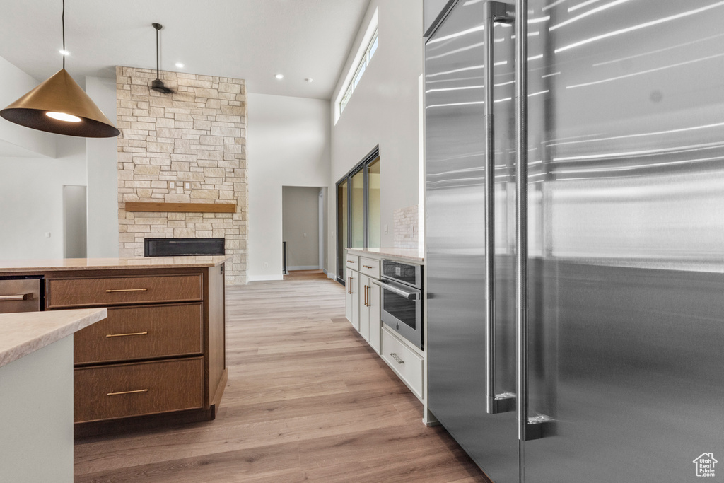 Kitchen with appliances with stainless steel finishes, a high ceiling, light wood-style floors, a stone fireplace, and decorative light fixtures