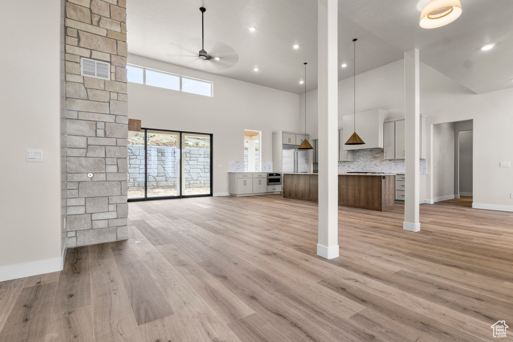 Unfurnished living room with high vaulted ceiling, a ceiling fan, light wood-type flooring, and recessed lighting