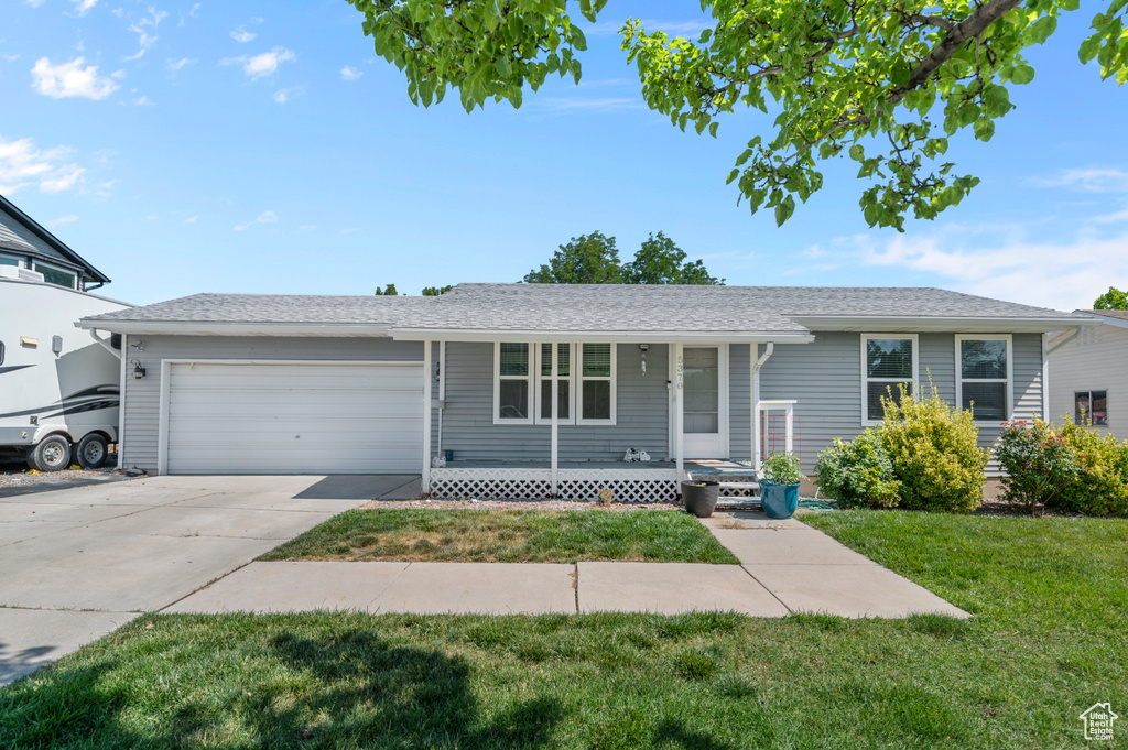Ranch-style home with covered porch, an attached garage, a front lawn, and driveway