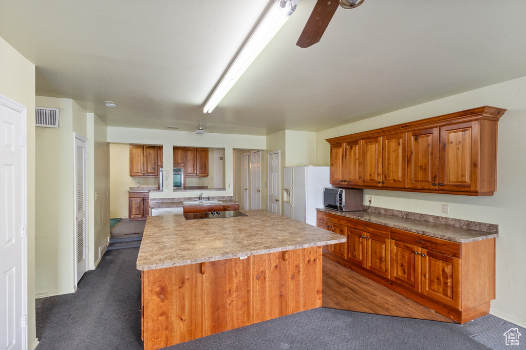 Kitchen featuring dark colored carpet, a center island, black electric cooktop, and brown cabinetry