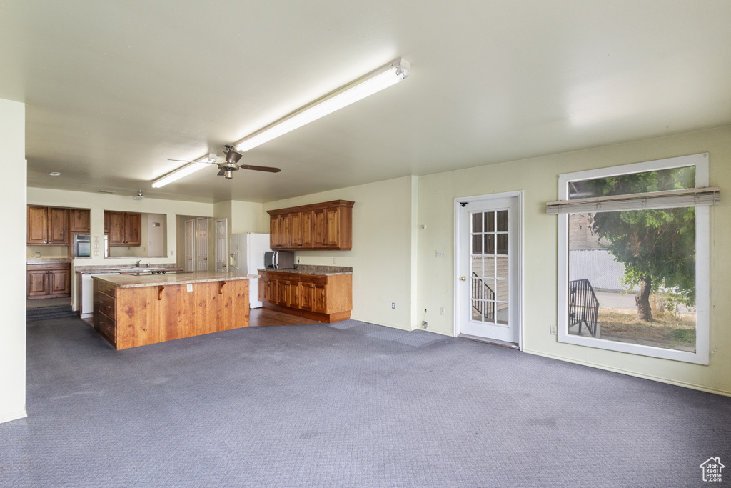 Kitchen with light countertops, a center island, brown cabinets, and dark carpet