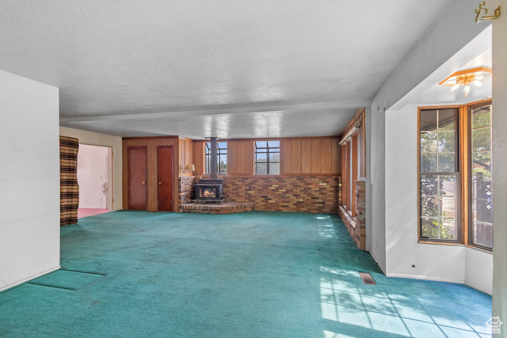 Unfurnished living room featuring carpet floors, a wood stove, and a textured ceiling