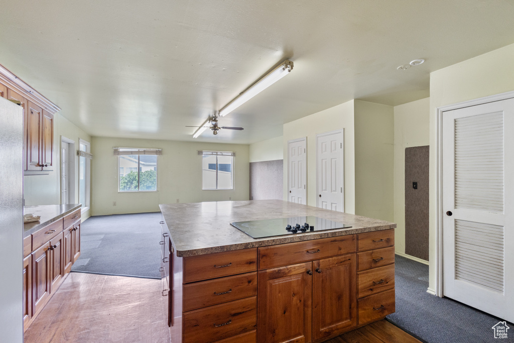 Kitchen featuring black electric cooktop, dark colored carpet, a ceiling fan, open floor plan, and a kitchen island