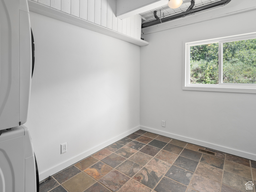 Washroom with estacked washer and dryer and dark stone finish floors