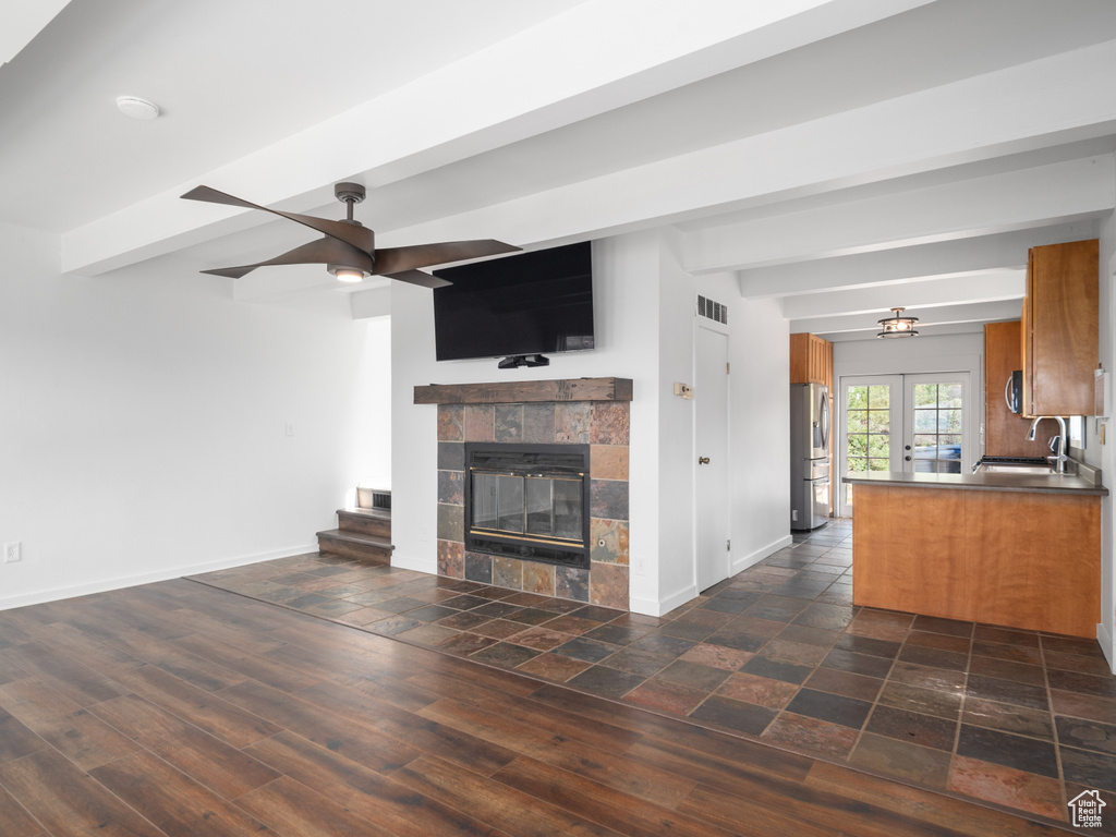 Unfurnished living room with ceiling fan, beamed ceiling, and a tiled fireplace