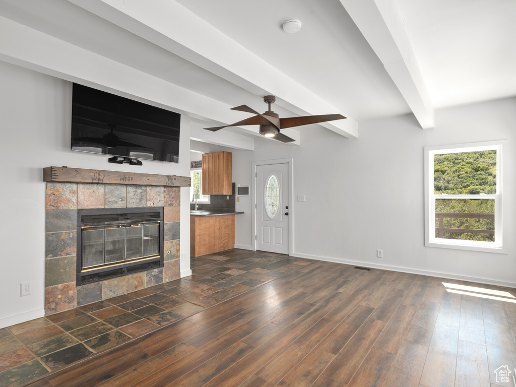 Unfurnished living room featuring beamed ceiling, a fireplace, ceiling fan, and dark wood-type flooring