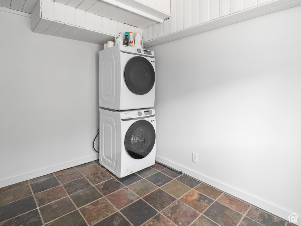 Laundry room with stacked washer and clothes dryer and stone tile flooring
