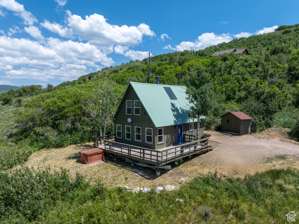 Rear view of property with a hot tub, a forest view, a shed, and a deck