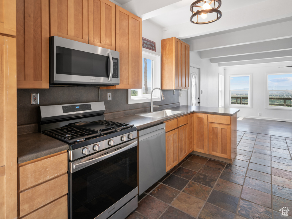 Kitchen featuring appliances with stainless steel finishes, stone tile floors, a peninsula, dark countertops, and backsplash