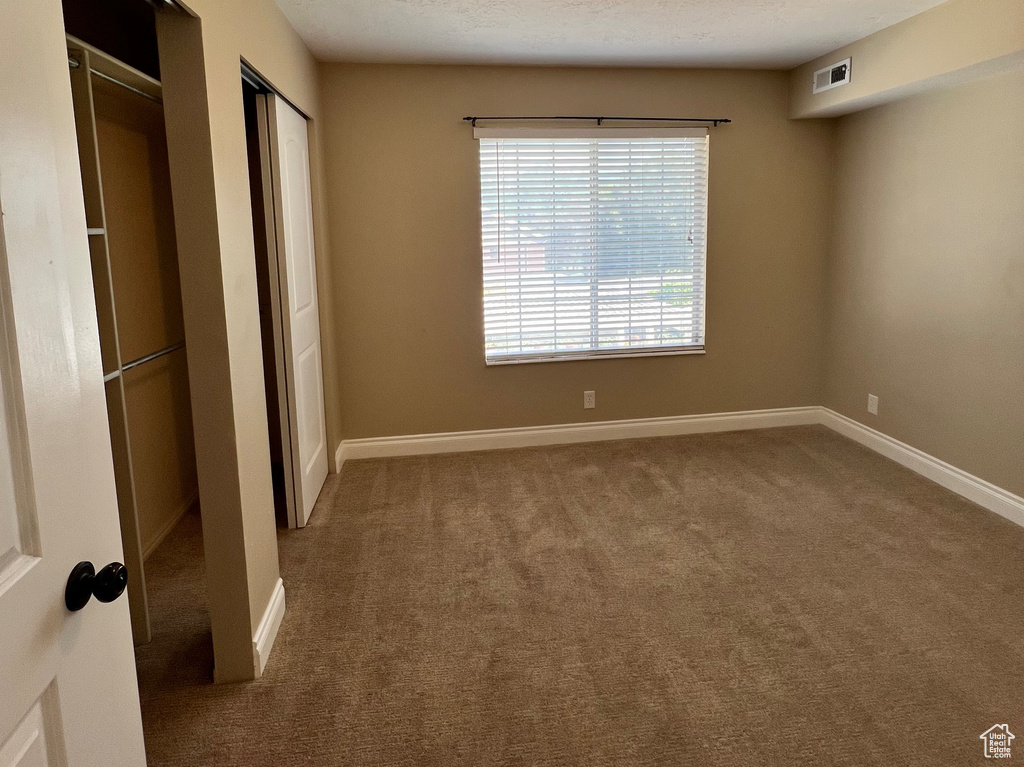 Unfurnished bedroom featuring carpet, a textured ceiling, and two closets