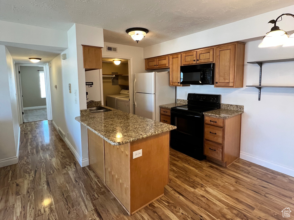 Kitchen with black appliances, brown cabinetry, dark wood finished floors, washing machine and dryer, and a peninsula
