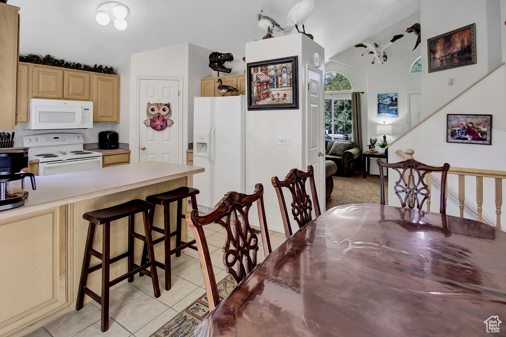 Kitchen featuring white appliances, light tile patterned floors, lofted ceiling, a kitchen breakfast bar, and light brown cabinetry