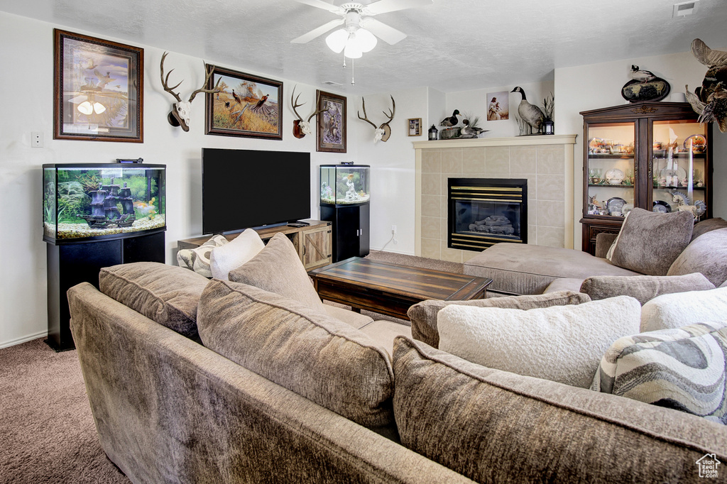 Carpeted living area with a tile fireplace, a ceiling fan, and a textured ceiling
