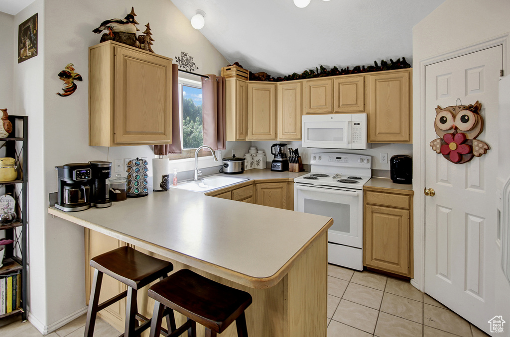 Kitchen featuring white appliances, light brown cabinetry, lofted ceiling, a kitchen breakfast bar, and a peninsula