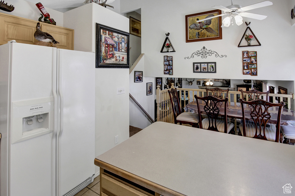 Kitchen featuring white fridge with ice dispenser, a ceiling fan, light brown cabinets, light tile patterned floors, and light countertops