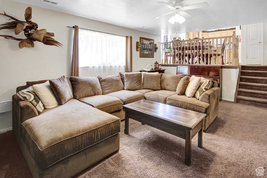 Carpeted living room with a ceiling fan and stairway