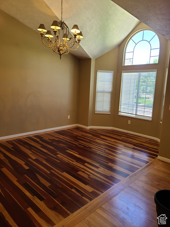 Spare room featuring wood-type flooring, vaulted ceiling, a chandelier, and a textured ceiling