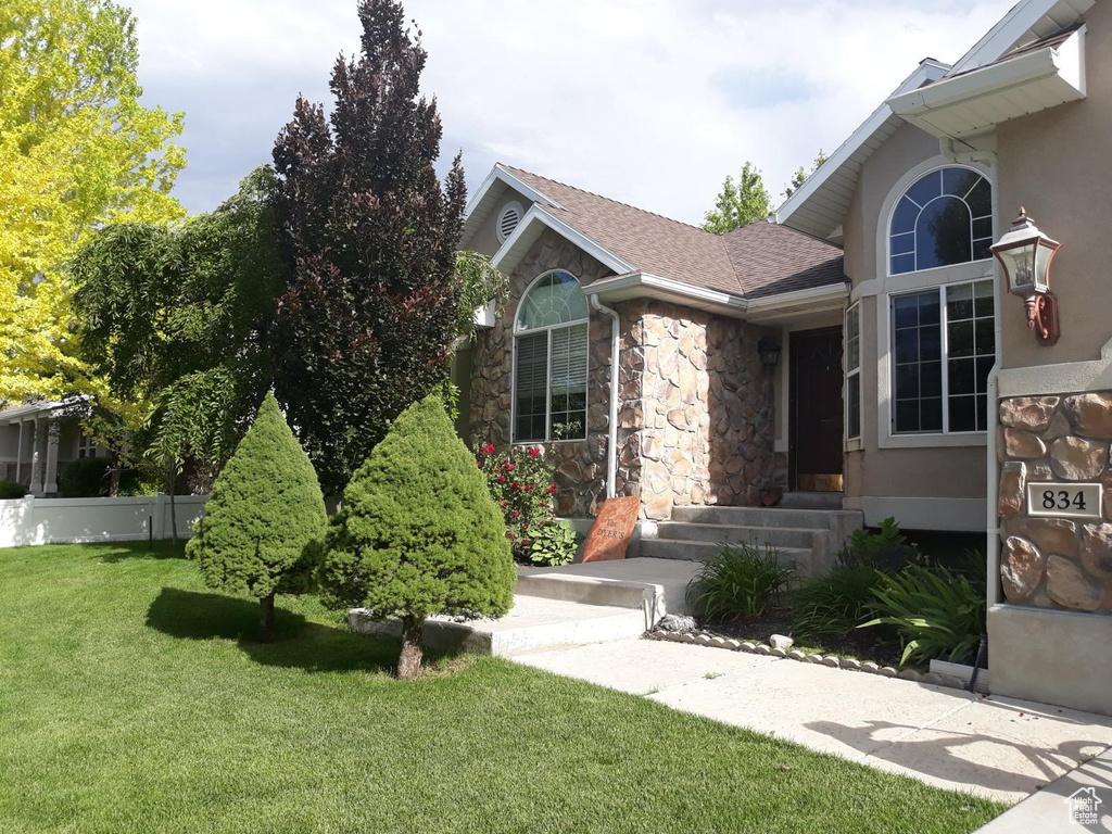 Doorway to property with stone siding, a yard, roof with shingles, and stucco siding