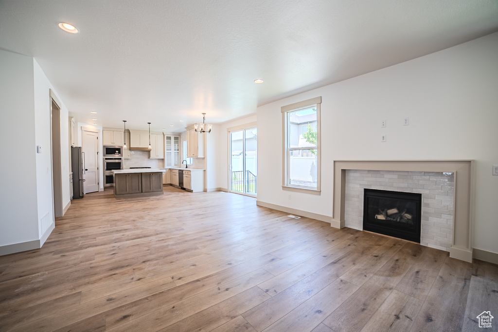 Unfurnished living room with a chandelier, light wood-style floors, a brick fireplace, and recessed lighting