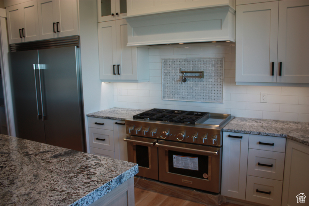 Kitchen featuring stainless steel appliances, custom exhaust hood, light stone countertops, and glass insert cabinets