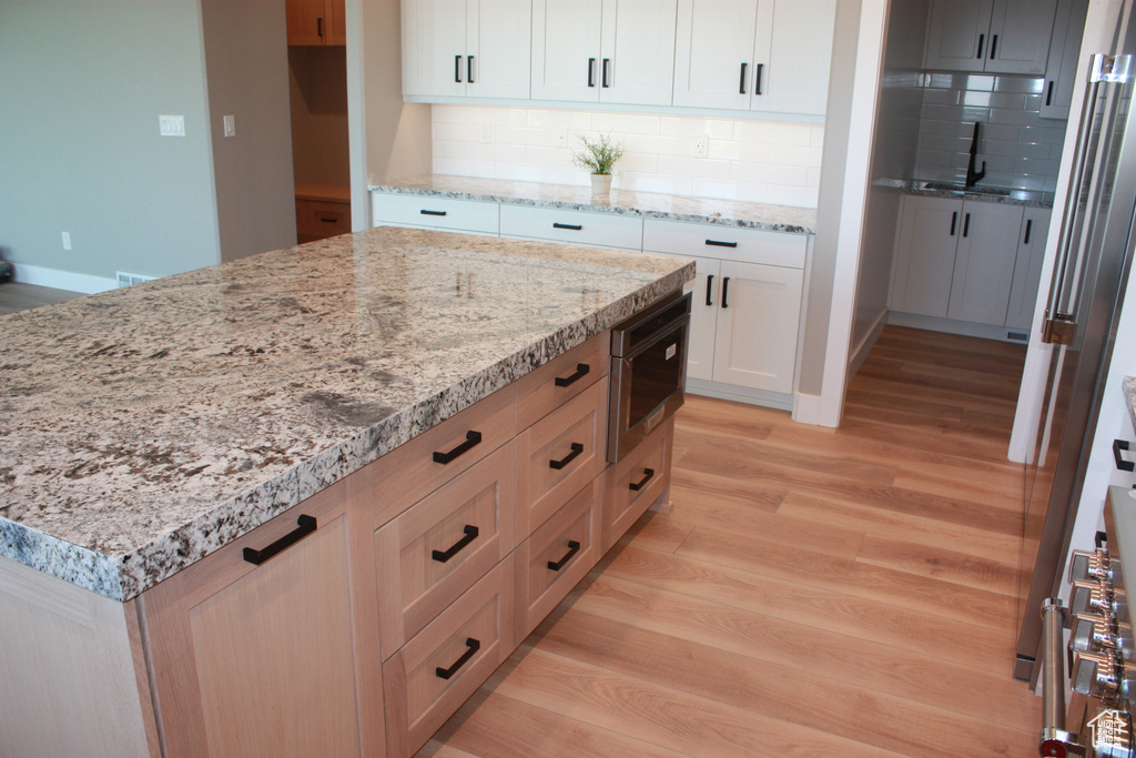 Kitchen with light wood-type flooring, tasteful backsplash, light stone counters, and white cabinets