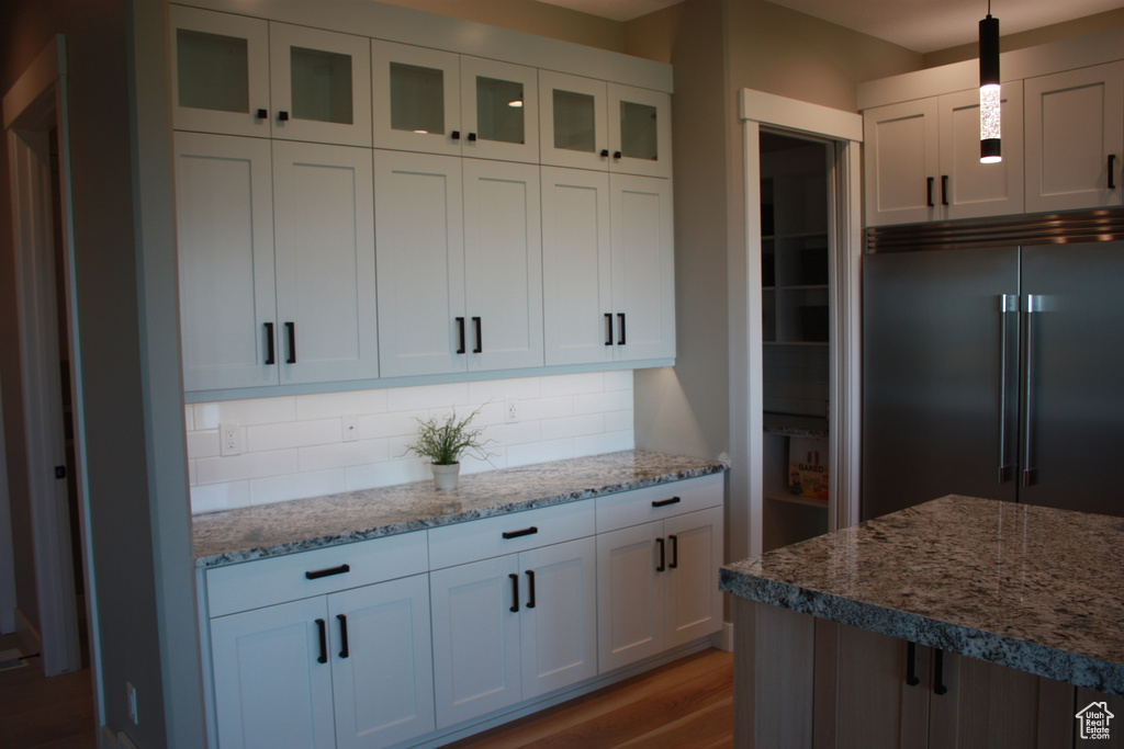 Kitchen with built in refrigerator, decorative backsplash, glass insert cabinets, and white cabinetry