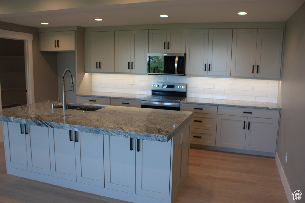 Kitchen featuring stainless steel appliances, light wood-style flooring, stone countertops, and recessed lighting