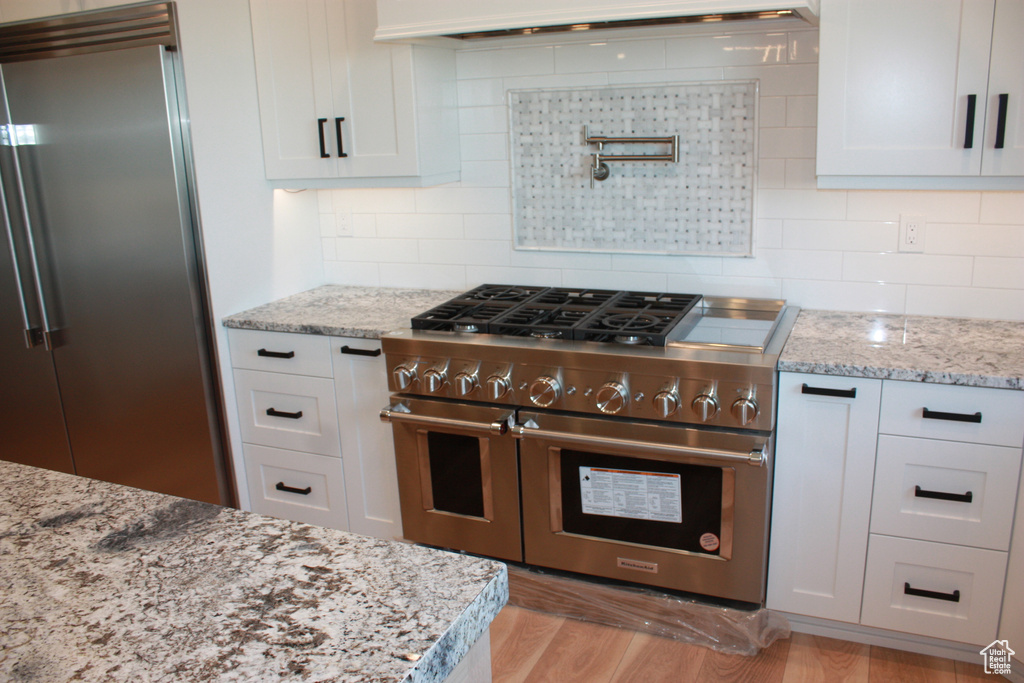 Kitchen with high end appliances, extractor fan, white cabinetry, and light wood-style flooring