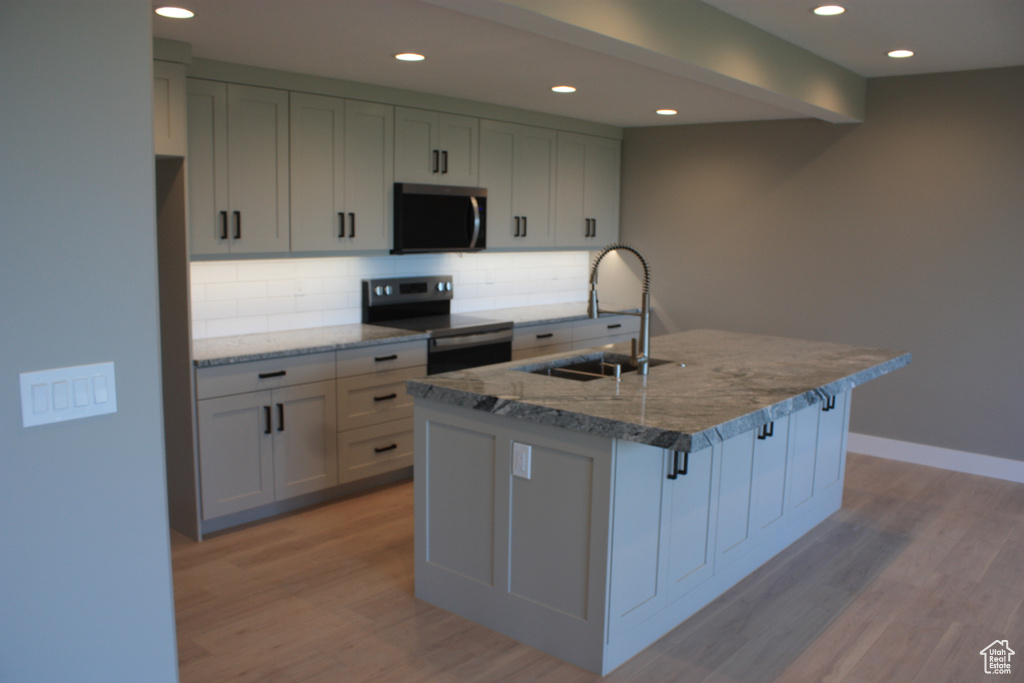 Kitchen featuring stainless steel electric stove, tasteful backsplash, light wood-style flooring, light stone counters, and recessed lighting