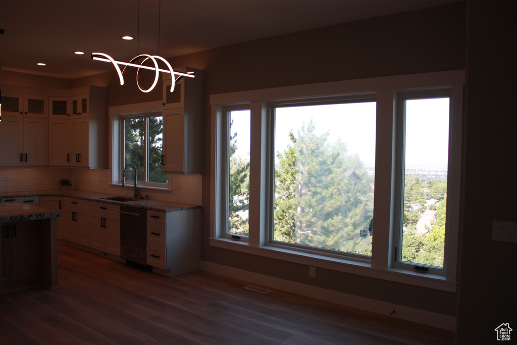 Kitchen with dishwashing machine, decorative backsplash, wood finished floors, white cabinetry, and light stone countertops