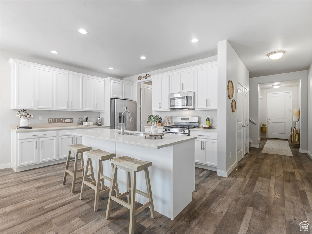 Kitchen with stainless steel appliances, light countertops, white cabinetry, an island with sink, and recessed lighting