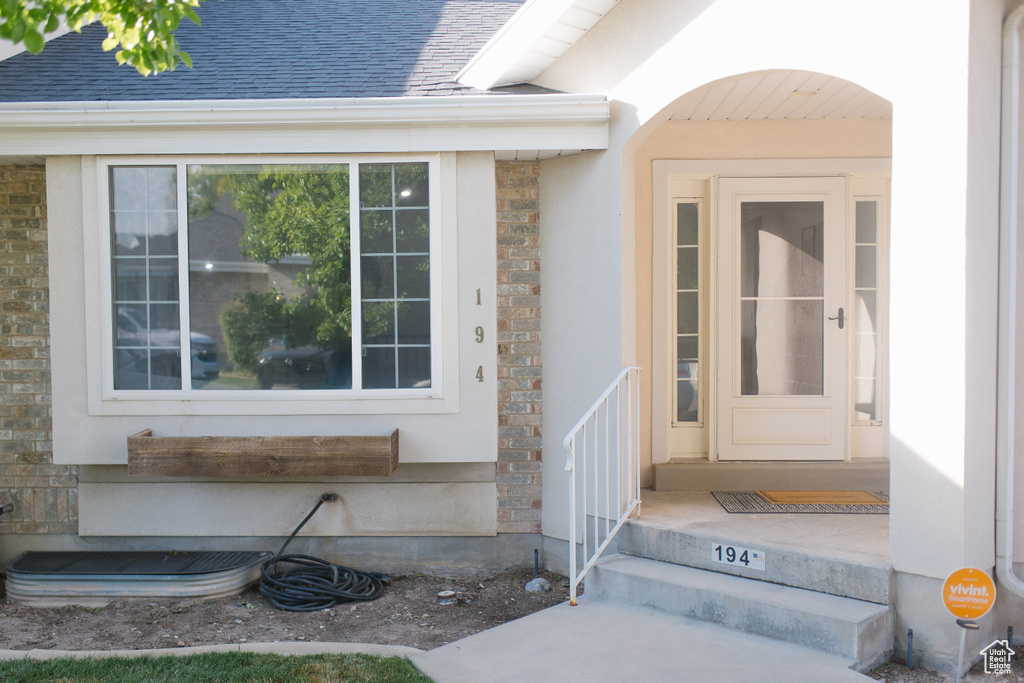 Doorway to property with stone siding, roof with shingles, and stucco siding