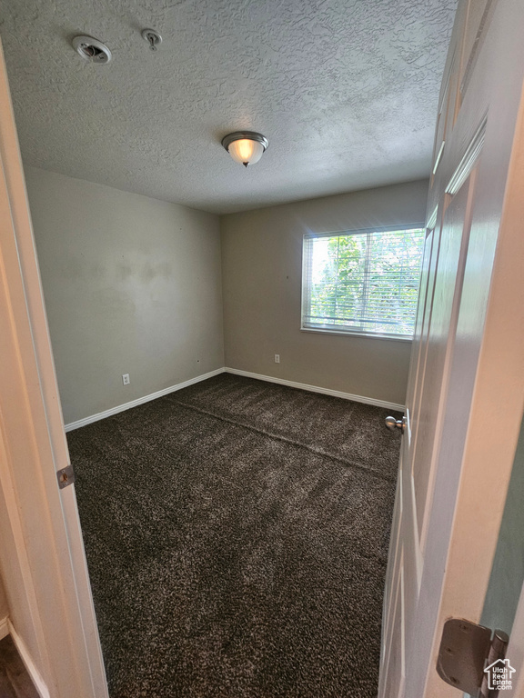 Unfurnished room featuring dark carpet and a textured ceiling