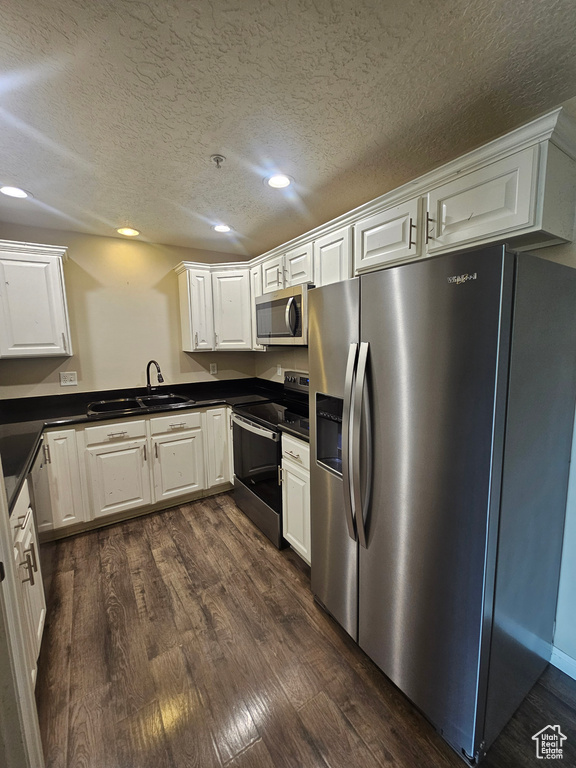Kitchen with stainless steel appliances, dark countertops, dark wood-style floors, white cabinets, and recessed lighting