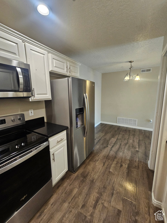 Kitchen with stainless steel appliances, dark countertops, dark wood-type flooring, white cabinets, and a chandelier