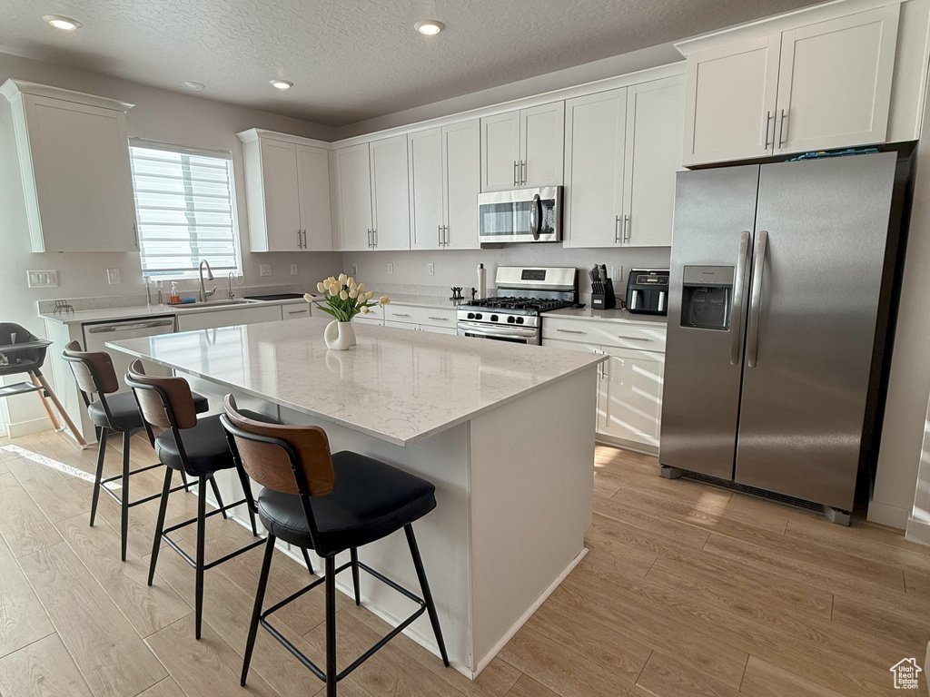 Kitchen featuring appliances with stainless steel finishes, light wood finished floors, a center island, white cabinets, and a textured ceiling