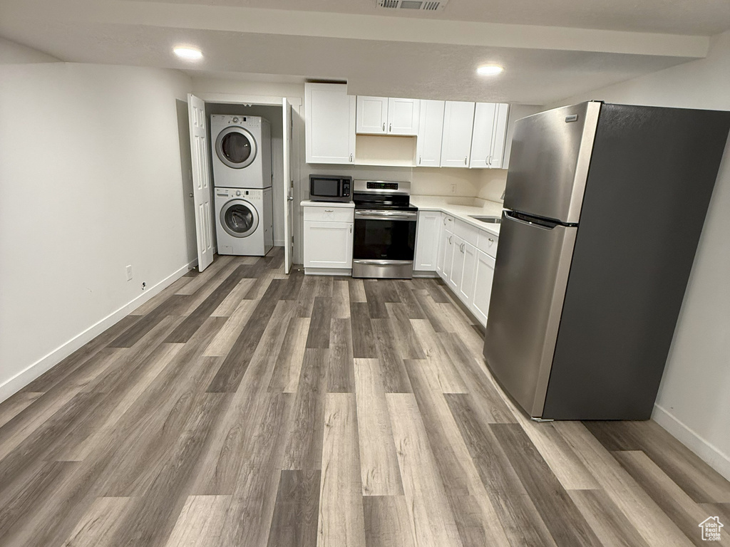Kitchen with stainless steel appliances, stacked washer / drying machine, white cabinets, and dark wood finished floors