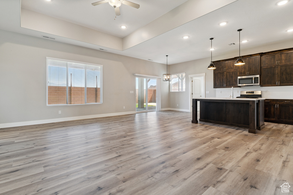 Kitchen with stainless steel microwave, stove, dark brown cabinets, light wood-type flooring, and ceiling fan