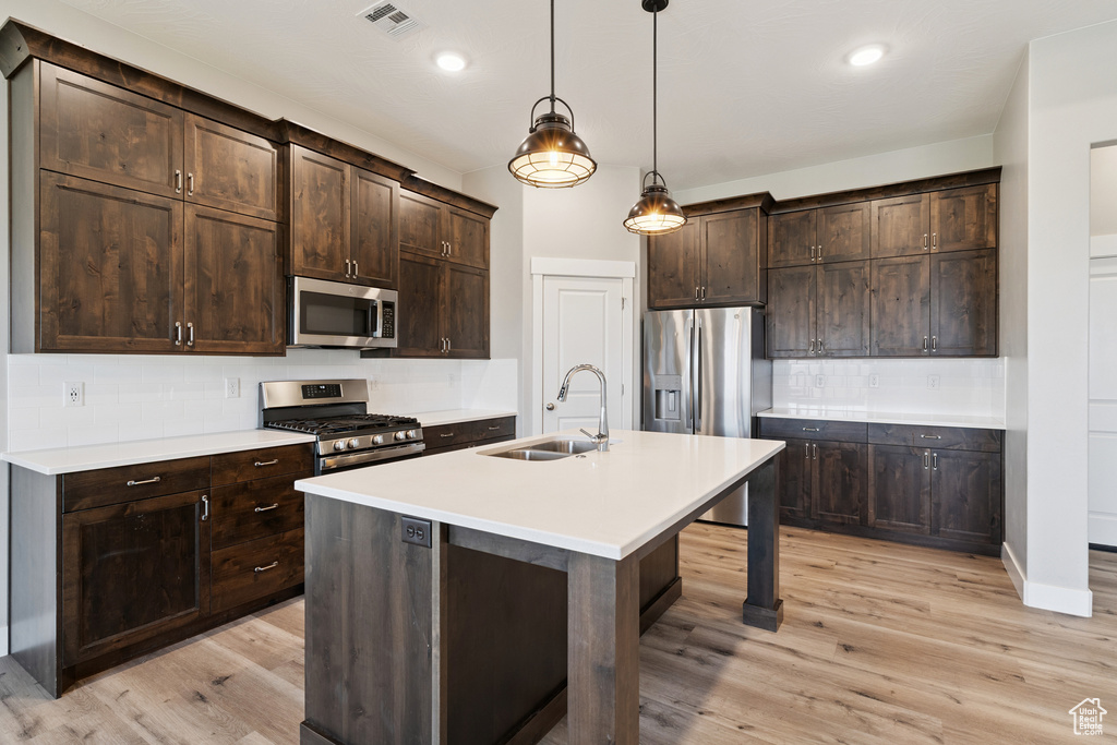 Kitchen with appliances with stainless steel finishes, backsplash, light wood-style flooring, dark brown cabinetry, and recessed lighting