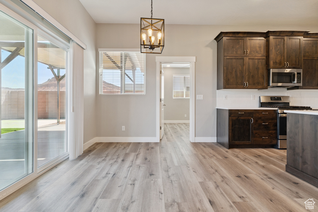 Kitchen featuring stainless steel appliances, dark brown cabinetry, a chandelier, and light wood finished floors