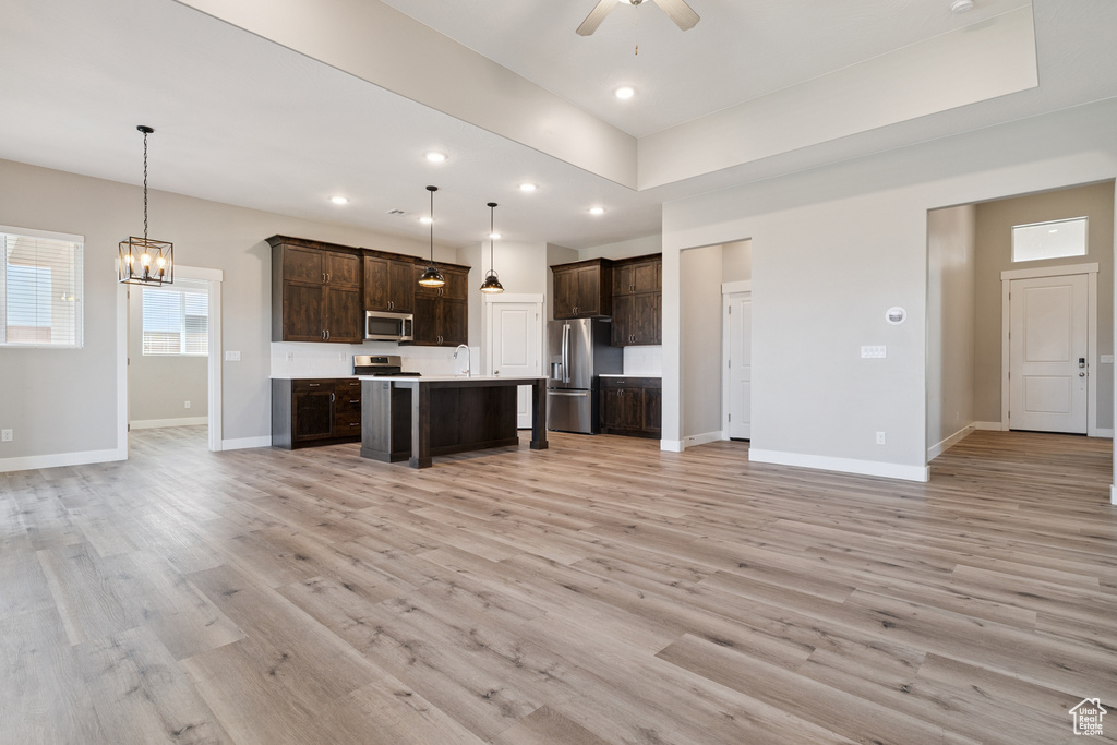 Kitchen featuring open floor plan, appliances with stainless steel finishes, dark brown cabinets, light countertops, and a chandelier