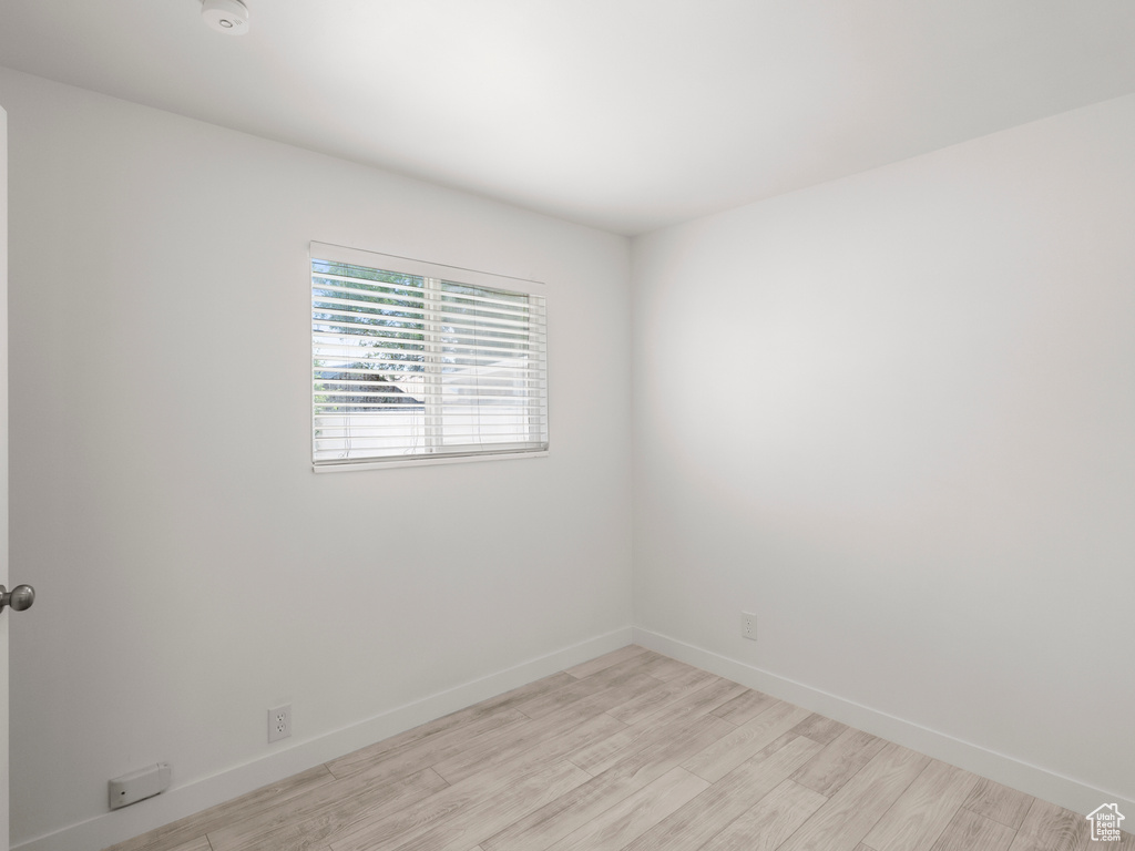 Empty room with light wood-style flooring and a smoke detector