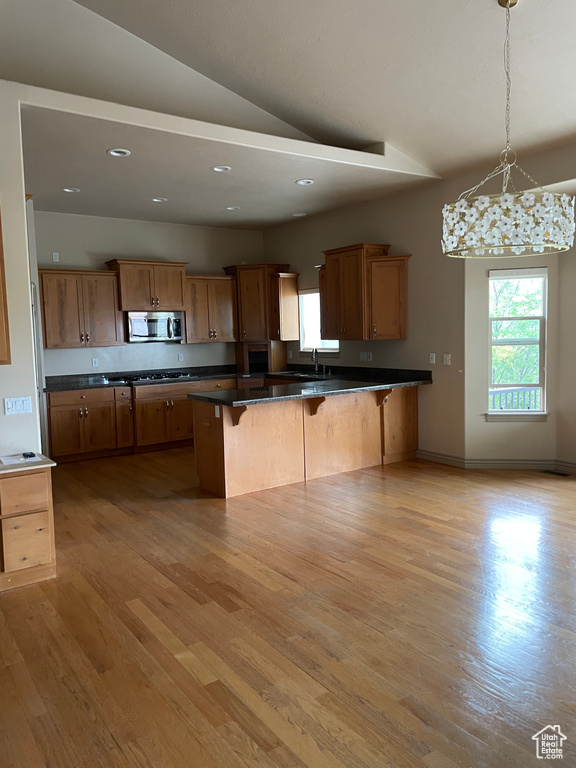 Kitchen with stainless steel microwave, a breakfast bar area, dark countertops, lofted ceiling, and light wood-type flooring