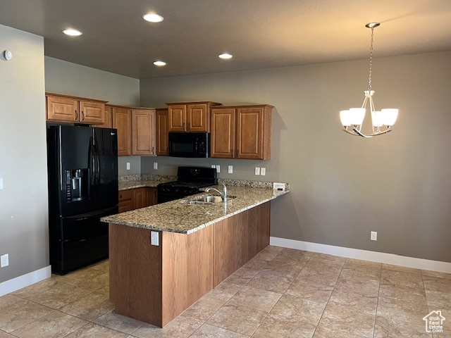 Kitchen featuring black appliances, a peninsula, brown cabinetry, a chandelier, and light stone counters