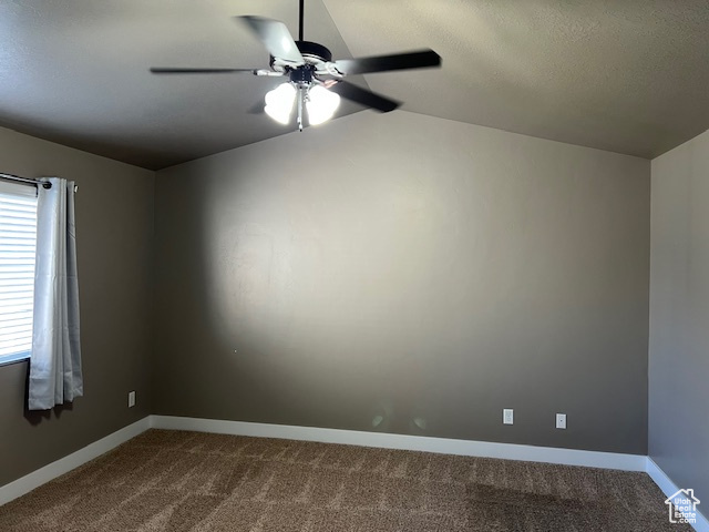 Empty room with dark carpet, a ceiling fan, vaulted ceiling, and a textured ceiling